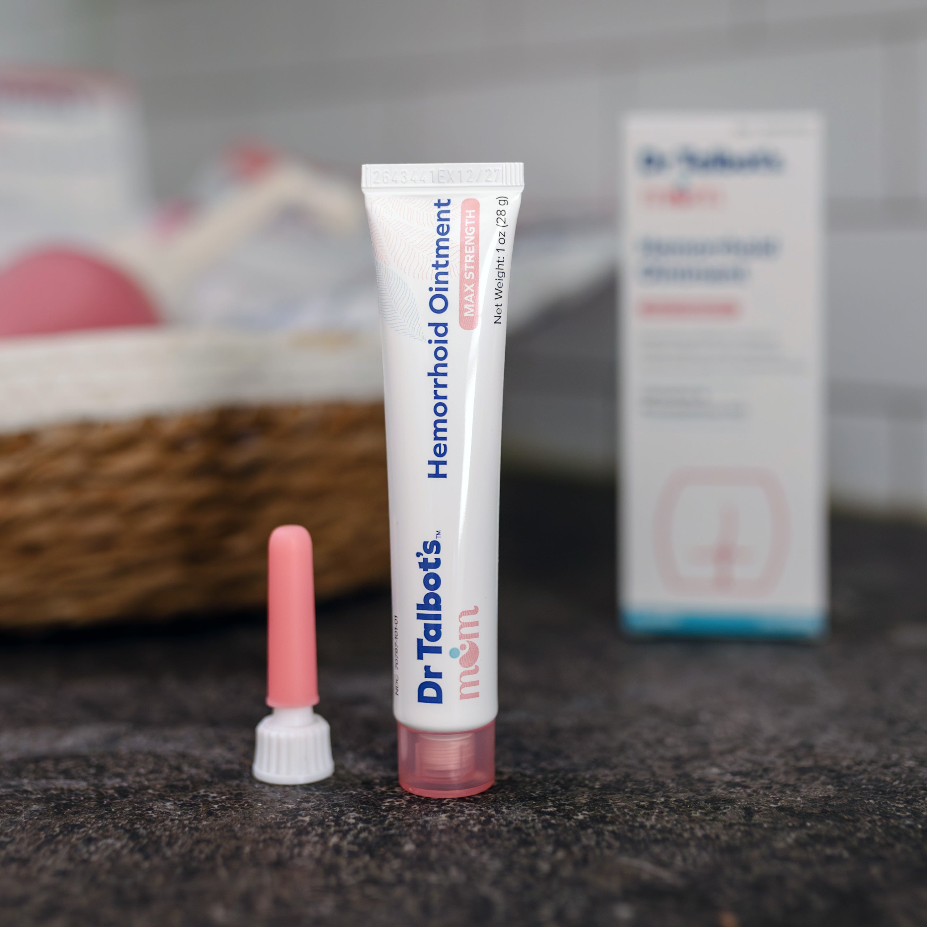 A tube of Dr. Talbot’s Mom Pregnancy & Postpartum Hemorrhoid Ointment with a pink cap, a separate pink applicator tip, and the product box in the background.