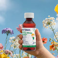 A hand holds a bottle of Dr. Talbot’s Daily Allergy Relief against a background of colorful wildflowers and a blue sky.
