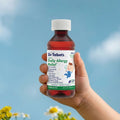A hand holds a bottle of Dr. Talbot’s Infant Daily Allergy Relief, with a label listing symptoms it treats, including hay fever, sneezing, and a runny nose.