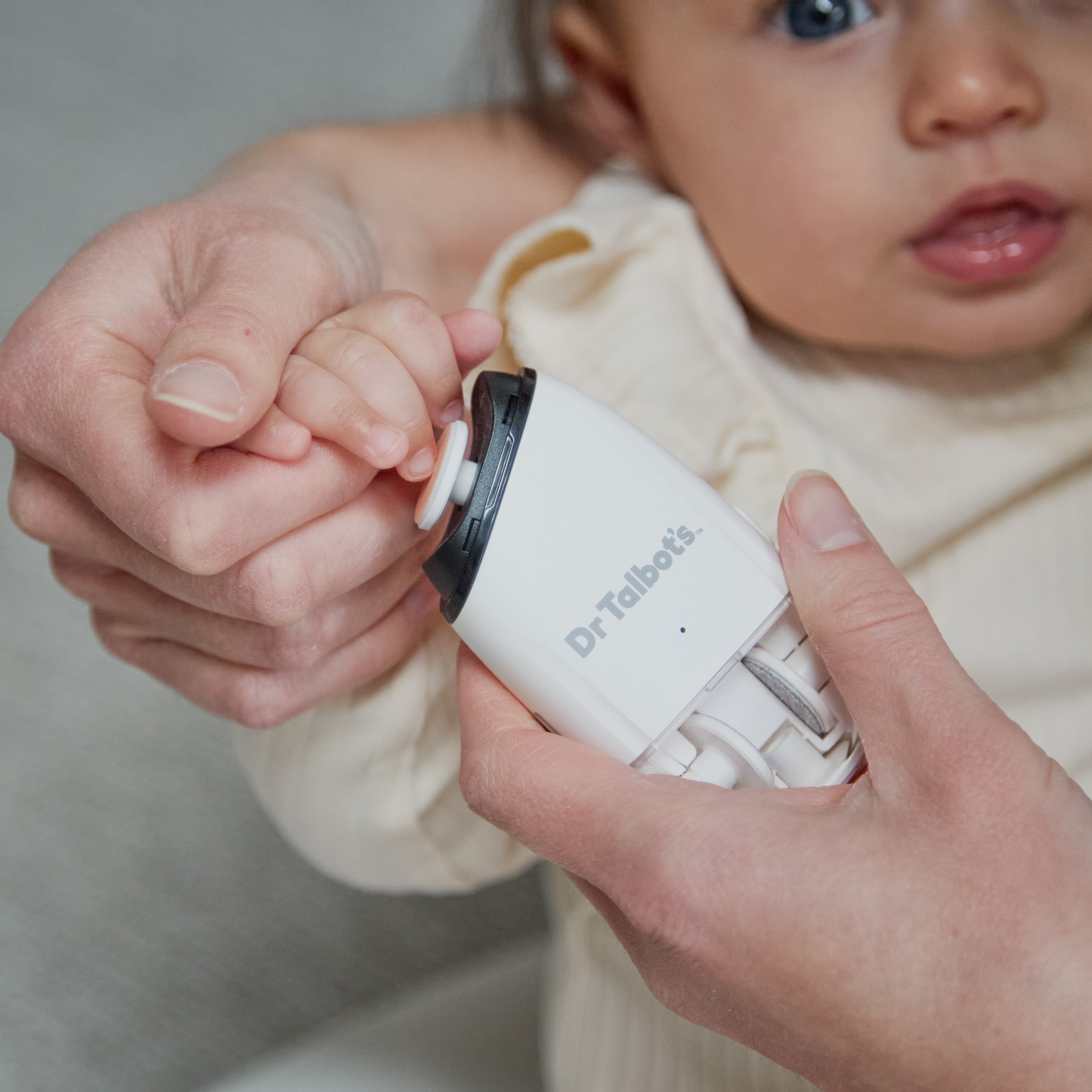 A hand holds a baby’s finger to a Dr. Talbot’s Portable Nail Trimmer with interchangeable heads.