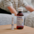 A bottle of Dr. Talbot’s Infant Cough Relief and an oral syringe standing on a wooden surface.