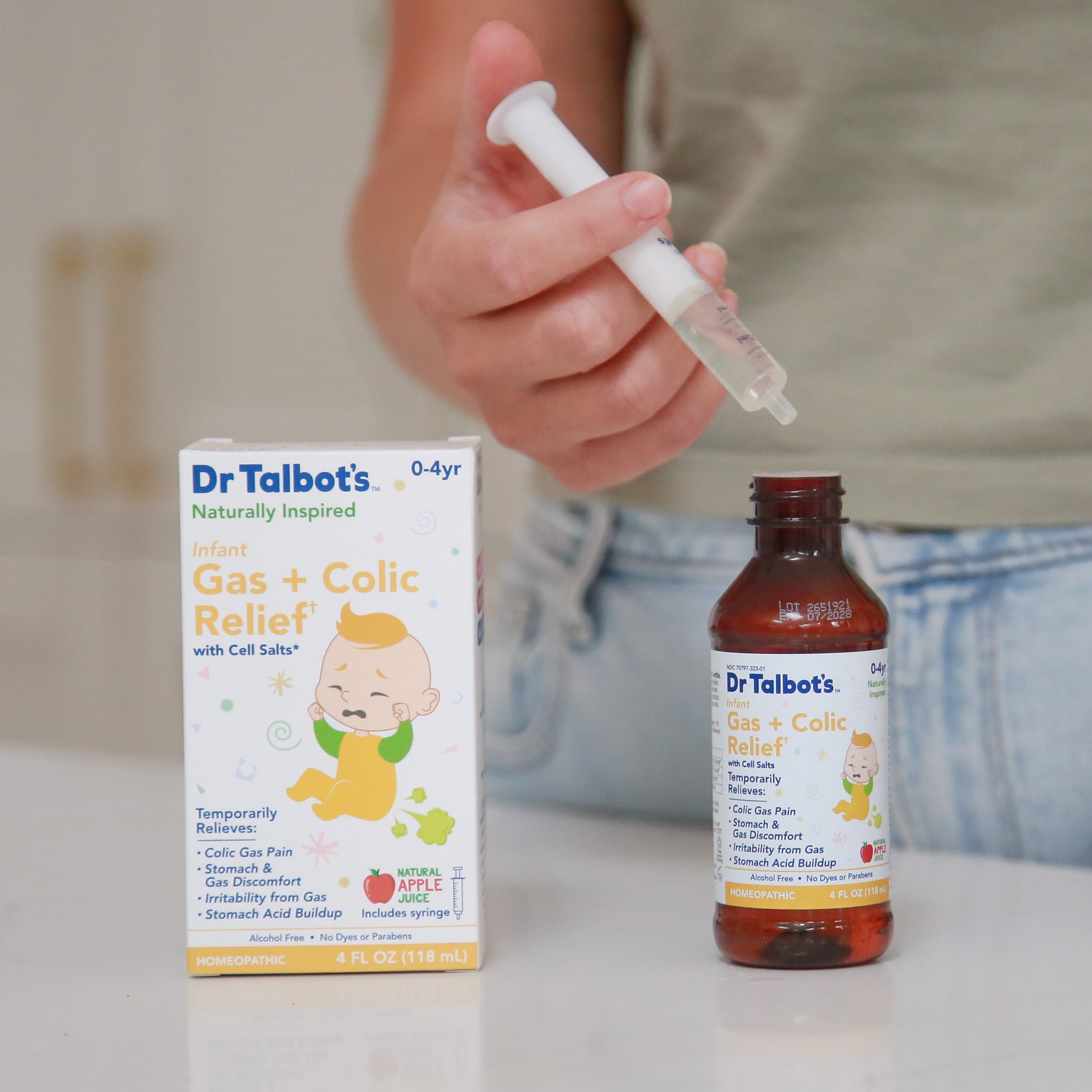 A person holds a dropper filled with liquid over an open bottle of Dr. Talbot’s Infant Gas + Colic Relief, with the product box standing next to it.