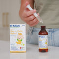 A person holds a dropper filled with liquid over an open bottle of Dr. Talbot’s Infant Gas + Colic Relief, with the product box standing next to it.