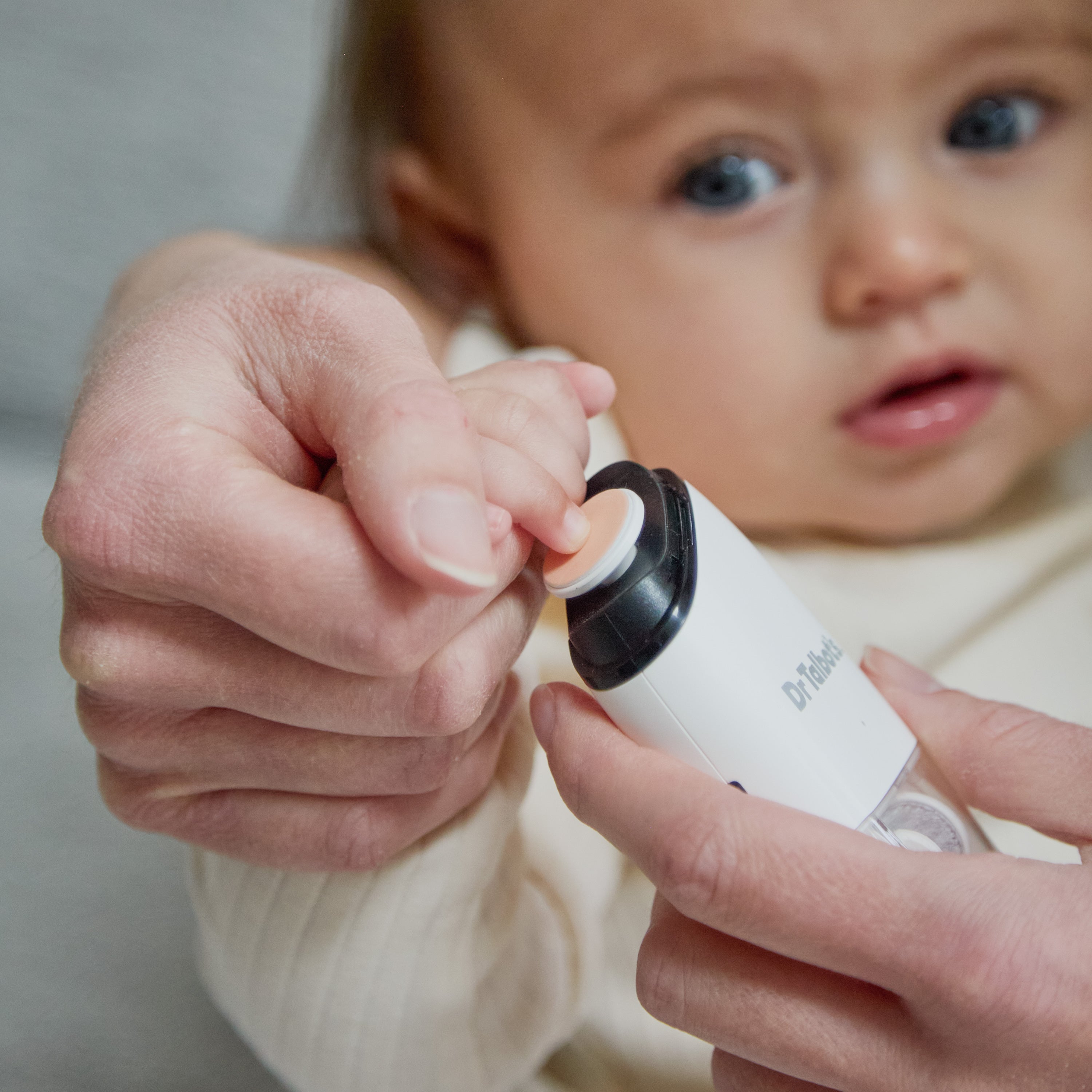 An adult uses a Dr. Talbot’s Portable Nail Trimmer with interchangeable heads to trim an infant’s fingernail.
