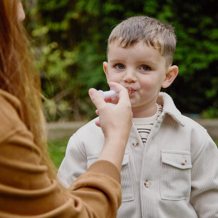 An adult uses a small oral syringe to administer liquid Dr. Talbot’s Infant Mucus + Cold Relief to a young child.