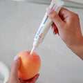 A hand squeezes a tube of Dr. Talbot’s Mom Pregnancy & Postpartum Hemorrhoid Ointment into the center of a peach.