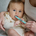 An adult holds a baby who is chewing on a light blue Dr. Talbot’s Sure-Dose™ Medicine Syringe used as an accurate dosage dispenser.