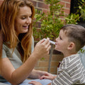 A woman uses an oral syringe to administer Dr. Talbot’s Infant Pain + Inflammation Relief to a young child.