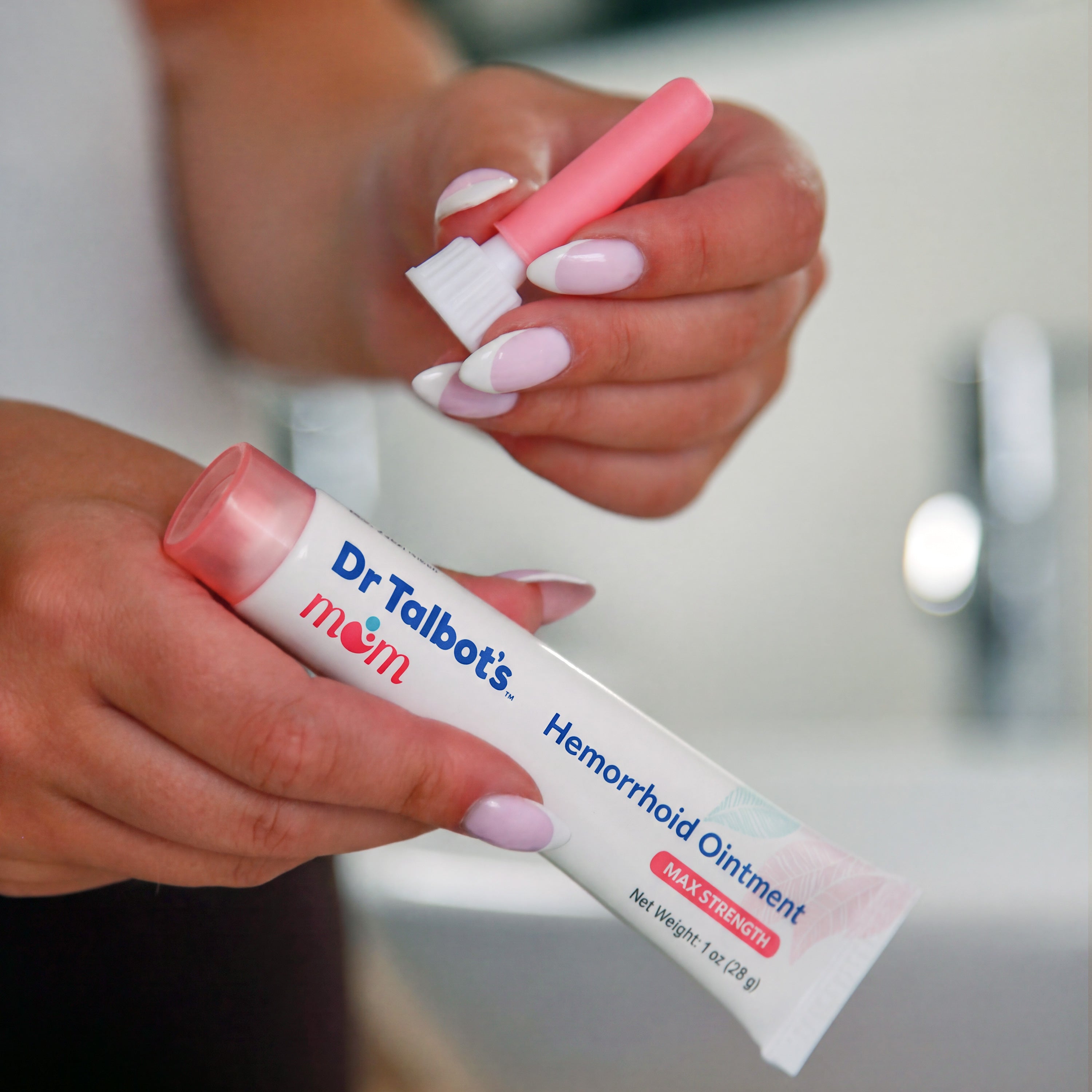 A person holds a tube of Dr. Talbot’s Mom Pregnancy & Postpartum Hemorrhoid Ointment and its matching pink applicator cap.