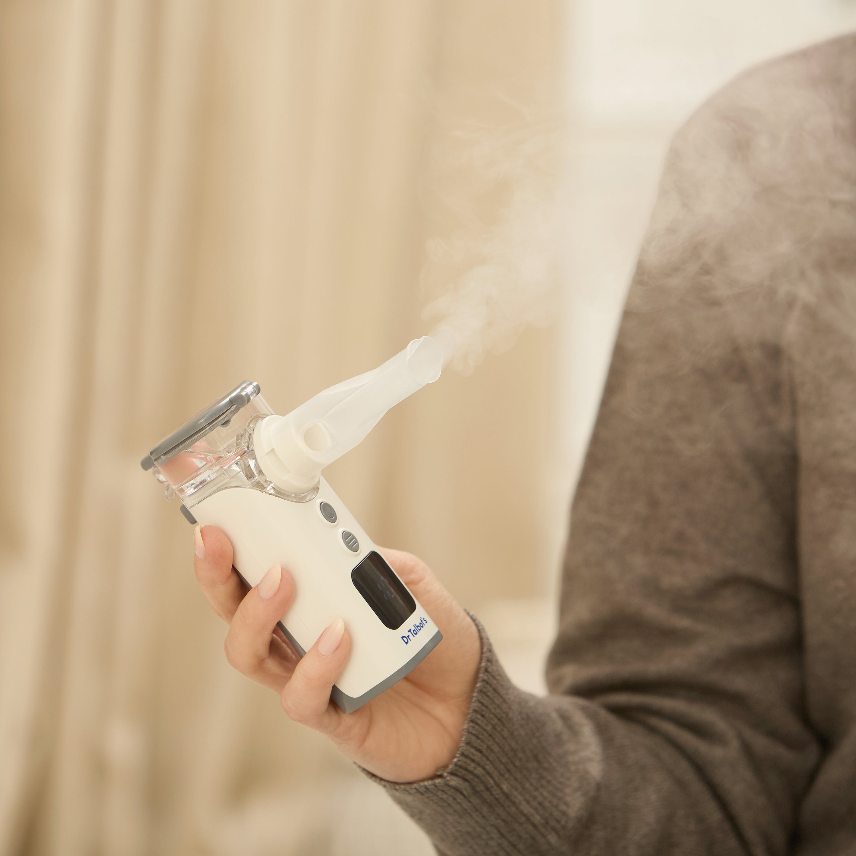 A person holds Dr. Talbot's Portable Ultrasonic Mesh Nebulizer emitting visible mist for respiratory relief, with part of their arm and torso seen in a softly lit indoor setting.