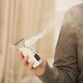 A person holds Dr. Talbot's Portable Ultrasonic Mesh Nebulizer emitting visible mist for respiratory relief, with part of their arm and torso seen in a softly lit indoor setting.