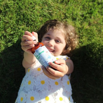 A young child lying on the grass holds a bottle of Dr. Talbot’s Infant Daily Allergy Relief toward the camera.