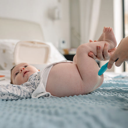 A baby lies on a blue textured blanket as an adult uses a blue applicator to apply Dr. Talbot's Diaper Rash Ointment | Original - 16 oz during a diaper change.