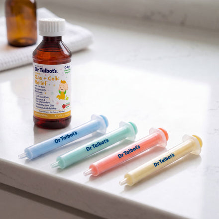 A Dr. Talbot’s Gas + Colic Relief bottle sits on a countertop beside four colorful Dr. Talbot’s Sure-Dose™ Medicine Syringes, each filled with different colored liquids for accurate dosage as baby medicine dispensers.