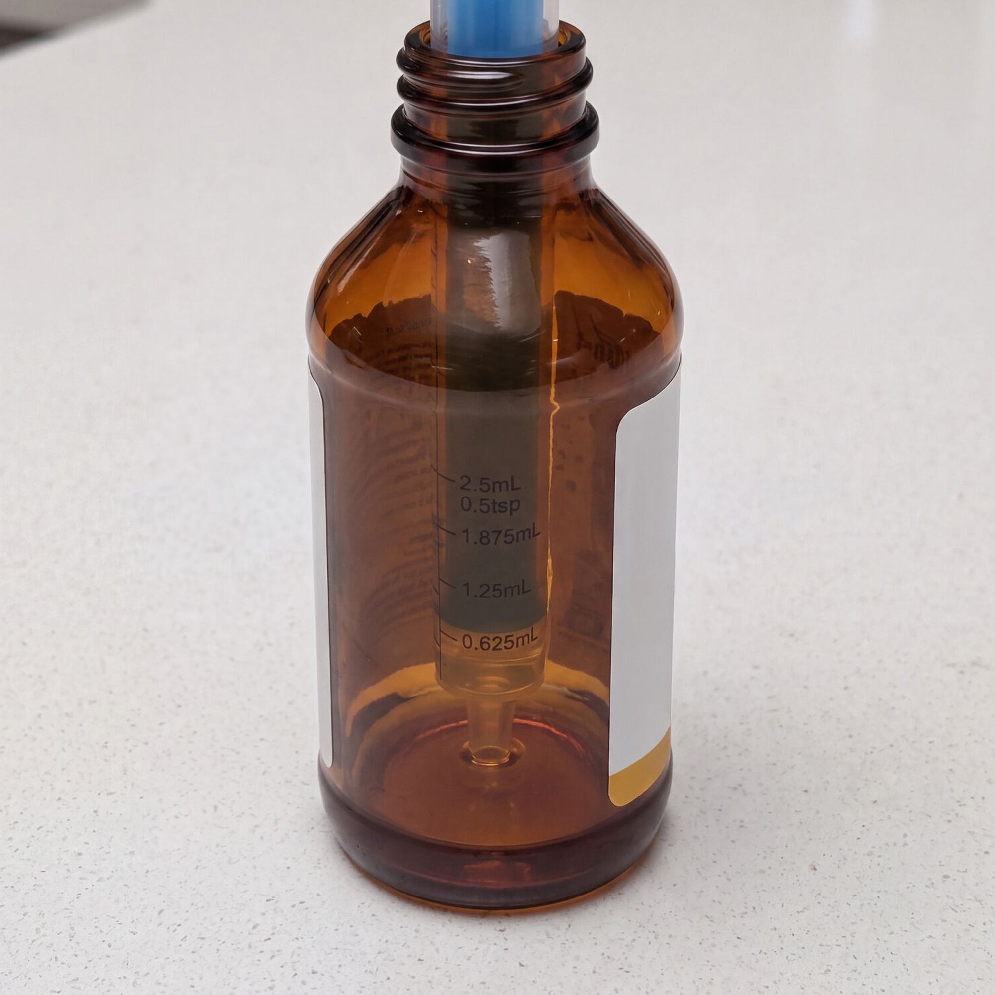 A Dr. Talbot’s Sure-Dose™ Medicine Syringe (4 Pack) is displayed, featuring a brown glass bottle with a blue dropper inside. The bottle has measurement markings from 0.625 mL to 2.5 mL on the side, allowing for accurate dosing when used as a baby medicine dispenser or along with medicine syringes. The background is a light-colored surface.