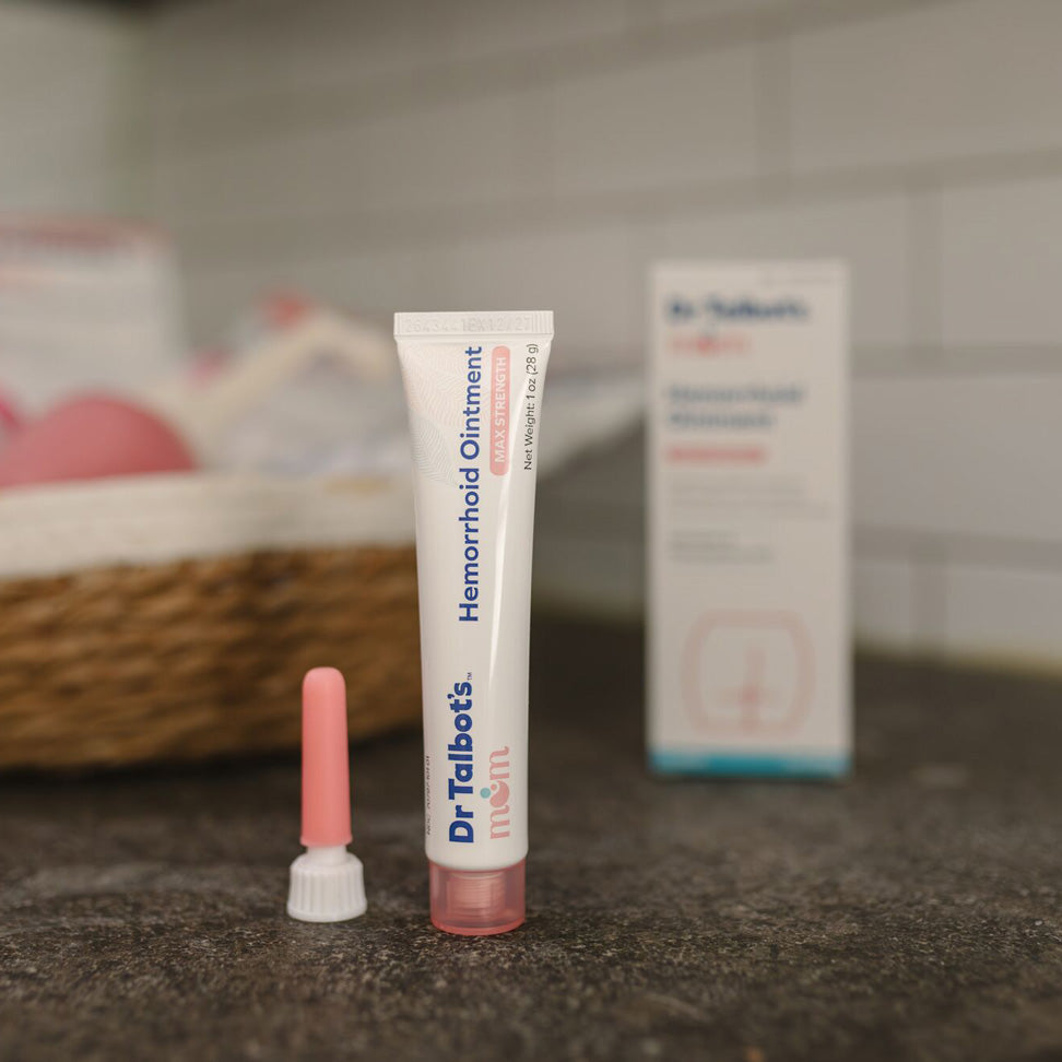 Dr. Talbot's Mom Pregnancy & Postpartum Hemorrhoid Ointment with a pink applicator and white cap is shown next to its box on a counter, offering gentle relief for pregnancy hemorrhoids.