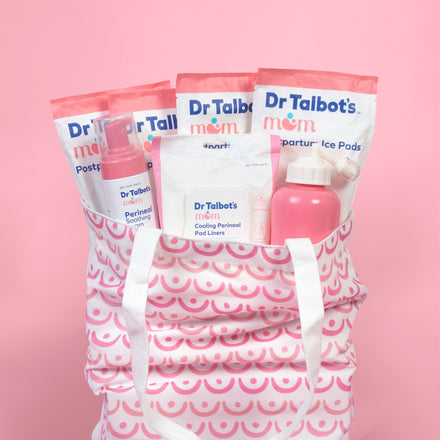 Dr. Talbot's Mom Postpartum Recovery Kit includes essentials like ice pads, perineal spray, pad liners, and a pink water bottle in a pink and white tote bag—ideal for perineal care after vaginal birth. Set against a pink background.