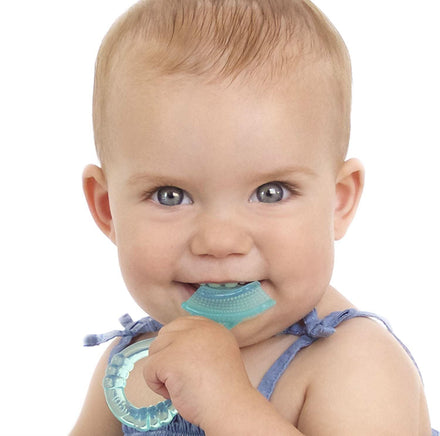 A light-skinned, blue-eyed baby smiles while holding Dr. Talbot's Soothing Gel + Massaging Toothbrush for teething relief, bringing it to their mouth. The baby wears a sleeveless outfit and sits against a white background.