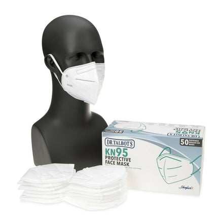A black mannequin head models a white KN95 mask with comfy ear loops. Beside it are stacks of unused masks and a Dr. Talbot's KN95 Cup Style Mask - 50 Pack box, emphasizing its 4-layer filter design for protection.